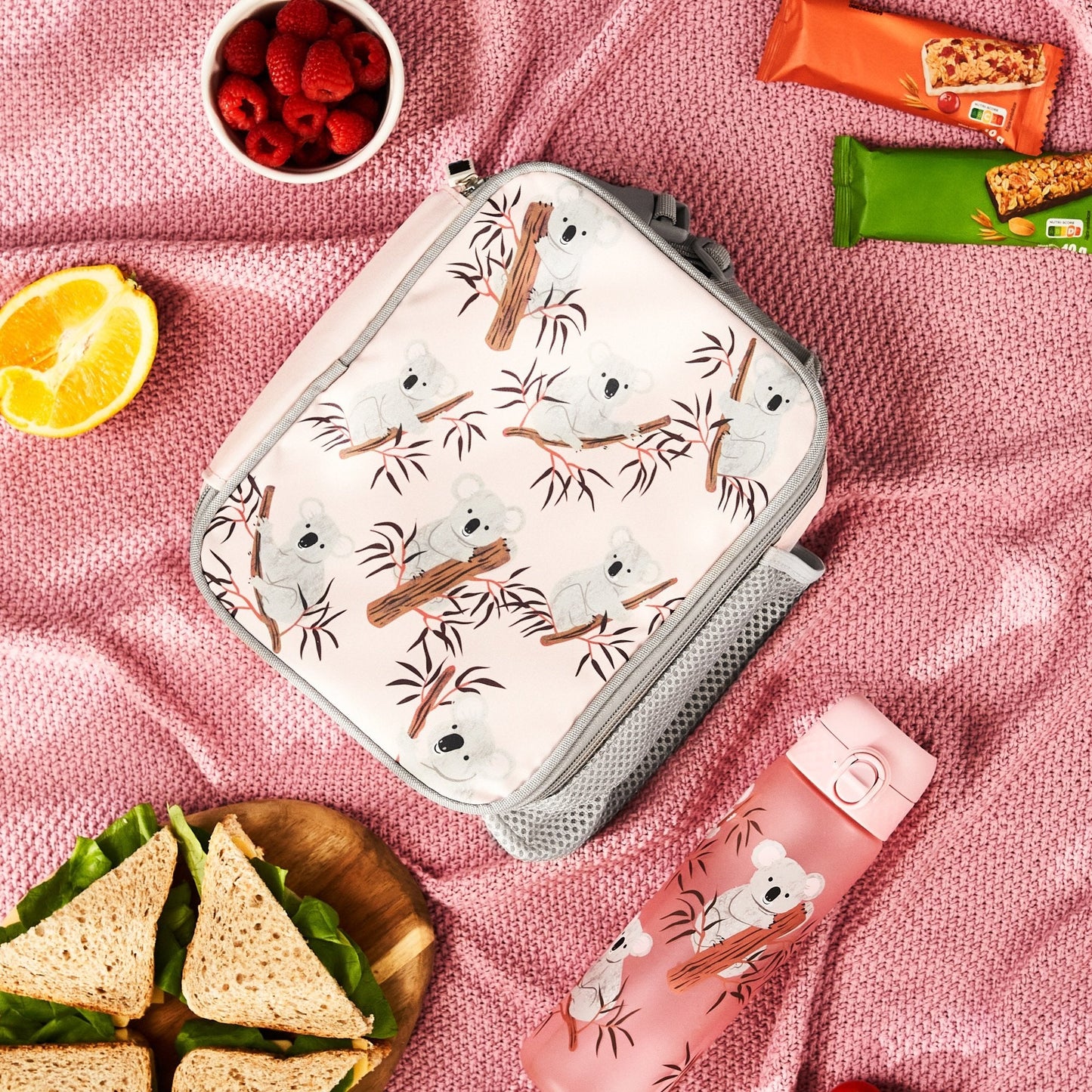 Lunch bag with koala design on a pink blanket with snacks and fruit