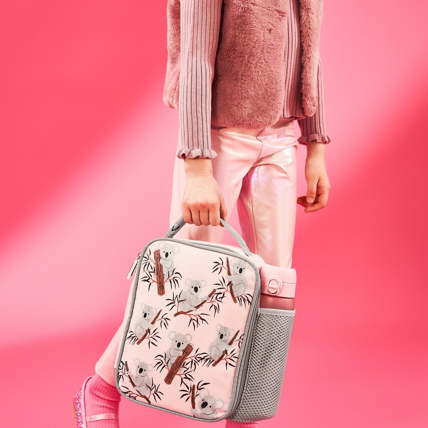 Person holding a pink lunch bag with koala design against a pink background