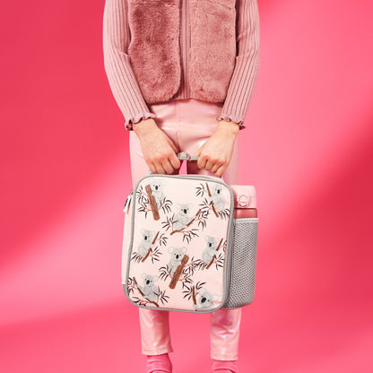 Person holding a pink lunch bag with koala design against a pink background