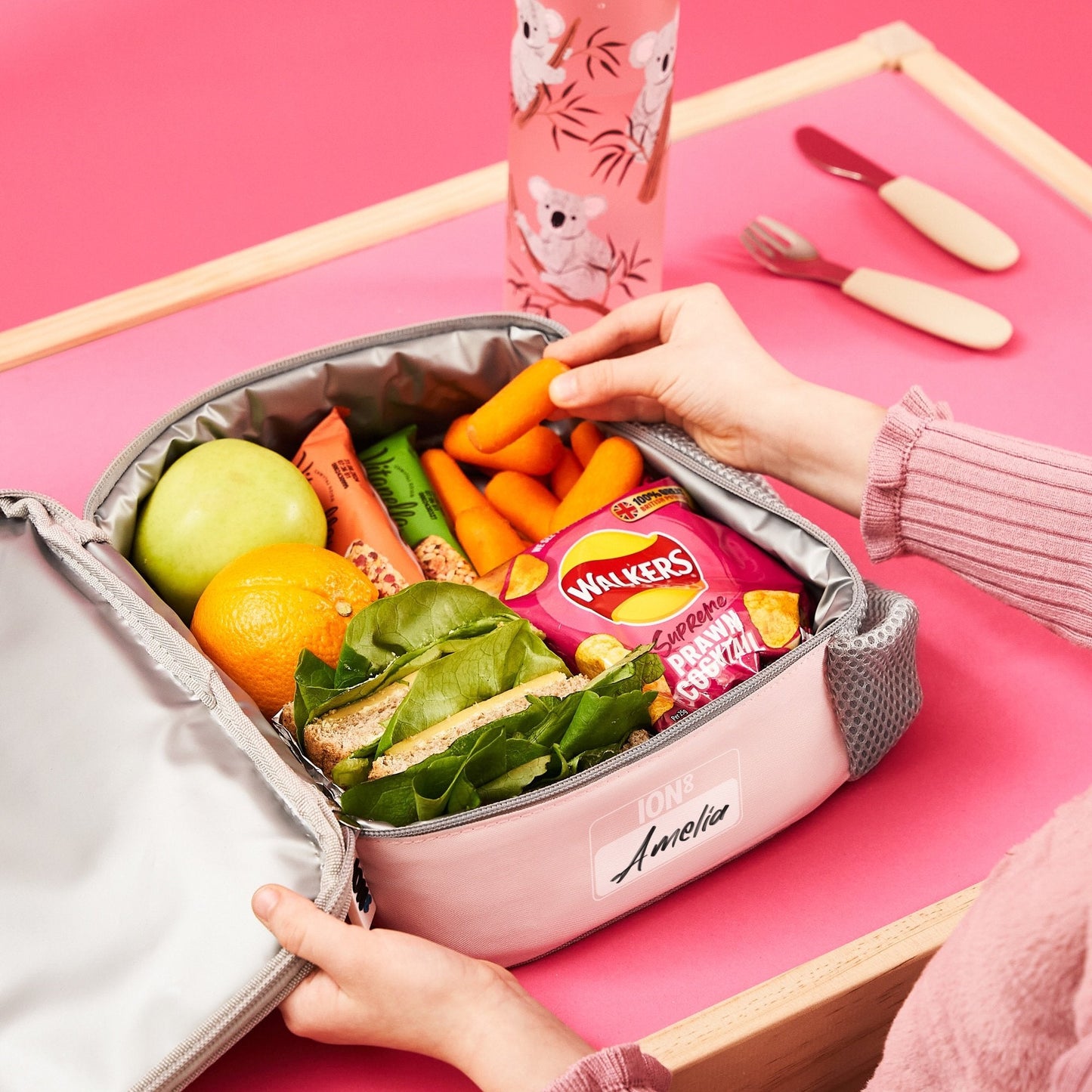 Pink lunch box with food items on a pink background