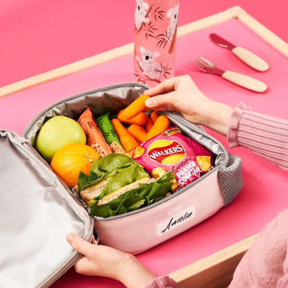 Pink lunch box with food items on a pink background