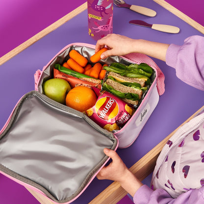 Person packing a lunchbox with vegetables, fruits, and snacks on a purple table.