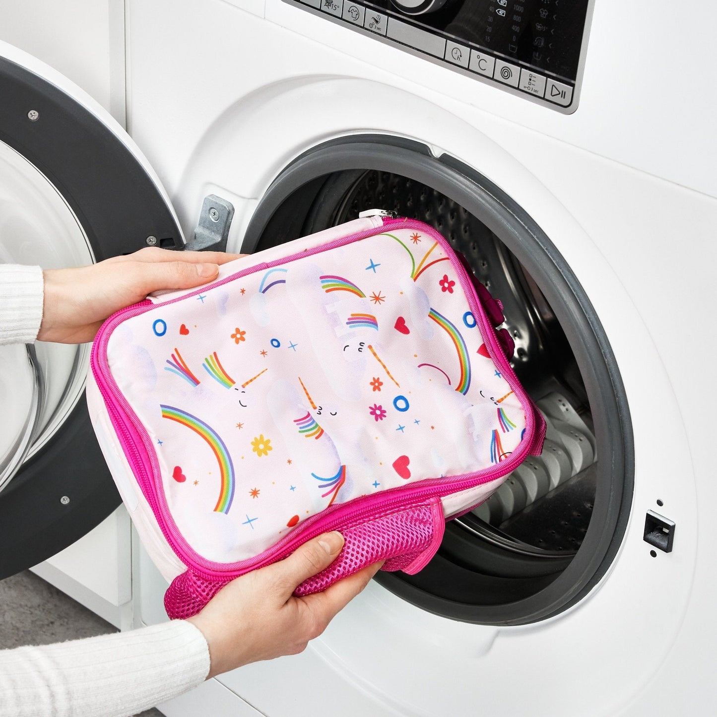 Person holding a pink and white pouch with colorful patterns in front of a washing machine.