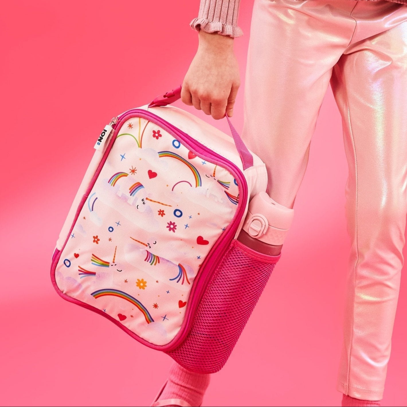 Pink lunch bag with colorful patterns held by a person against a pink background