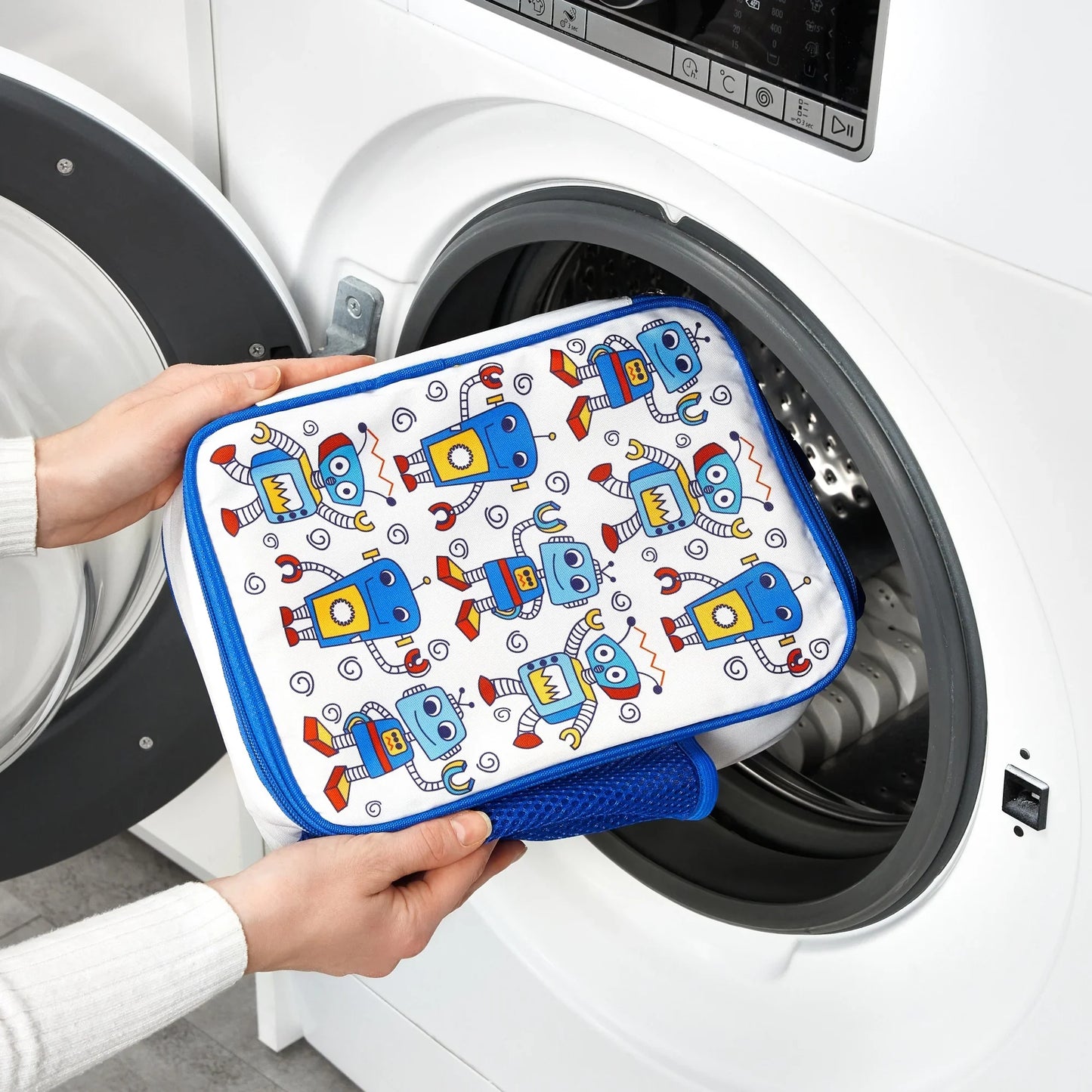 Person holding a robot-patterned pouch in front of a washing machine