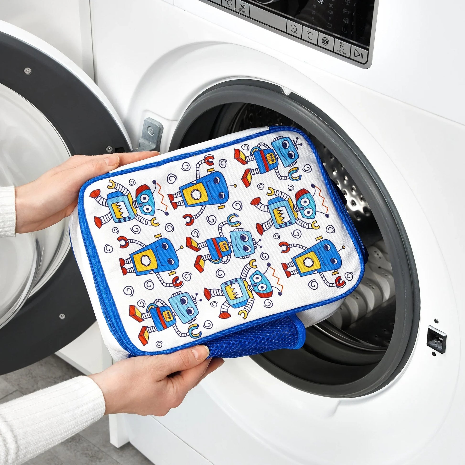 Person holding a robot-patterned pouch in front of a washing machine