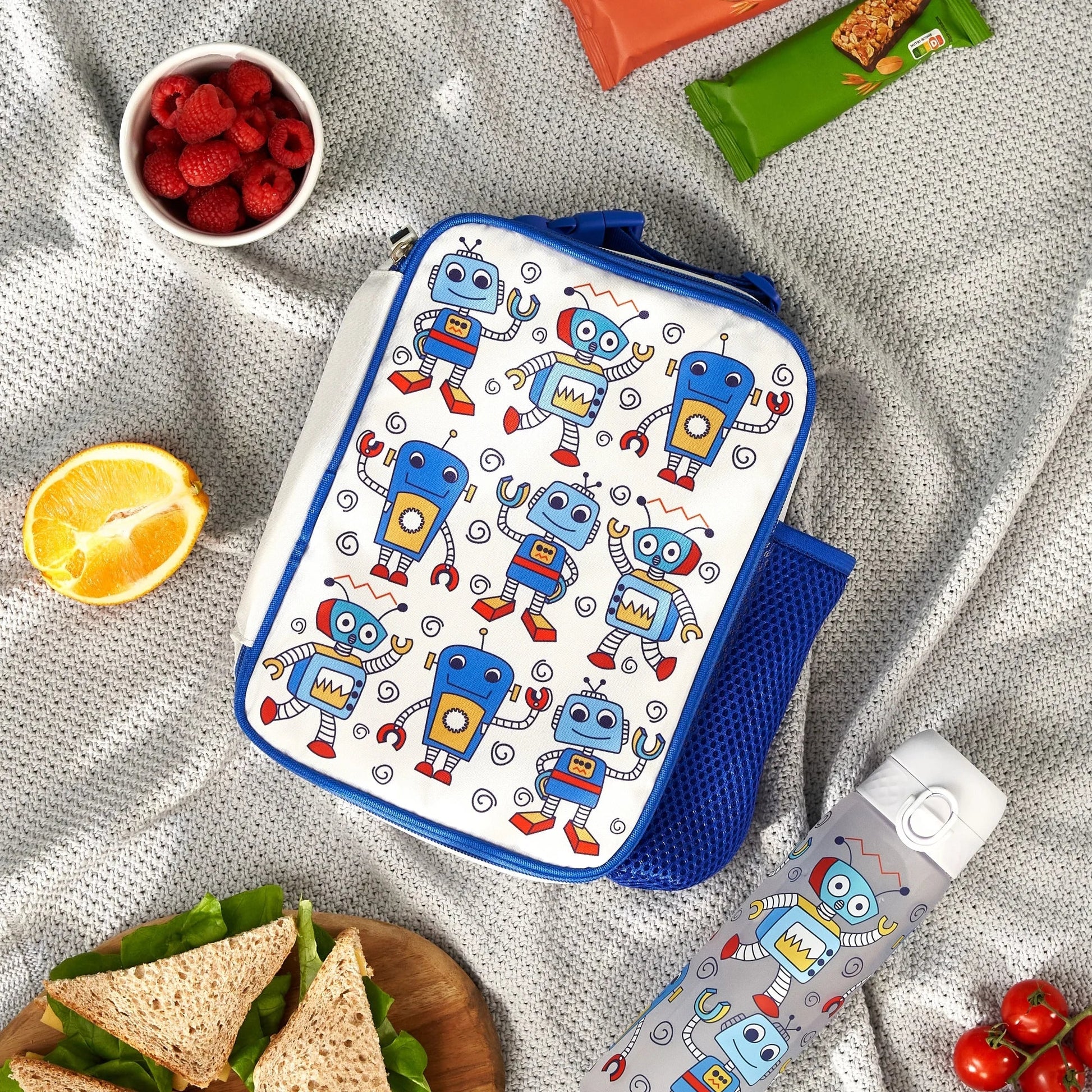 Lunch bag with robot pattern surrounded by snacks on a textured surface