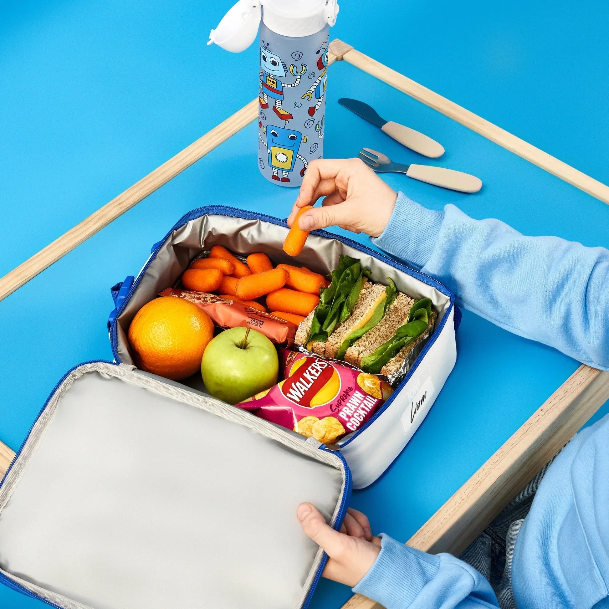 Lunchbox with food items including a sandwich, fruits, and a water bottle on a blue background.