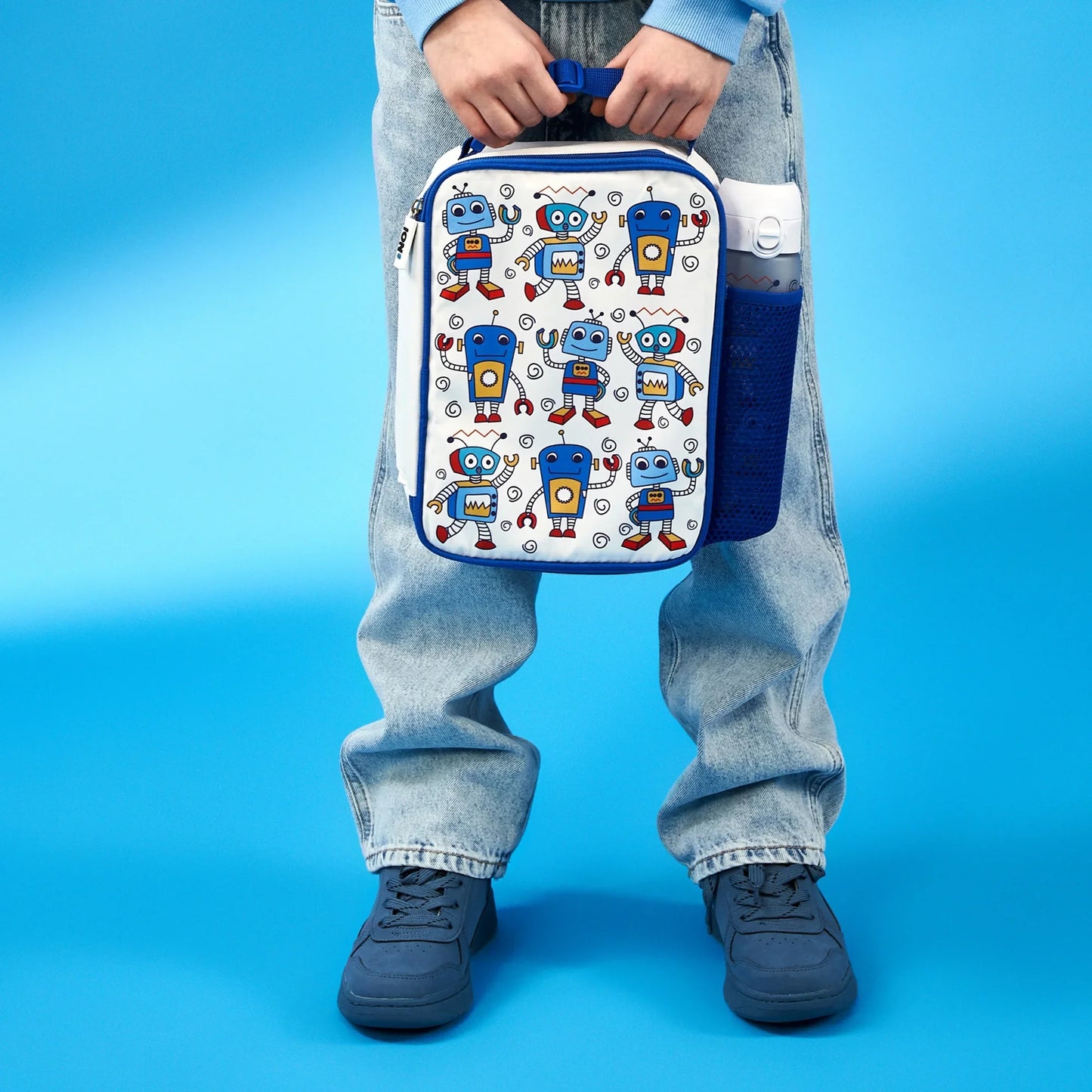 Person holding a robot-patterned lunch bag against a blue background