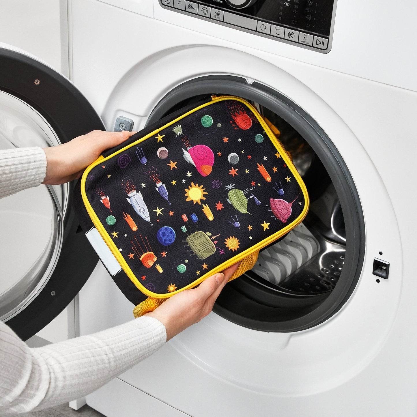 Person holding a space-themed pouch in front of an open washing machine.