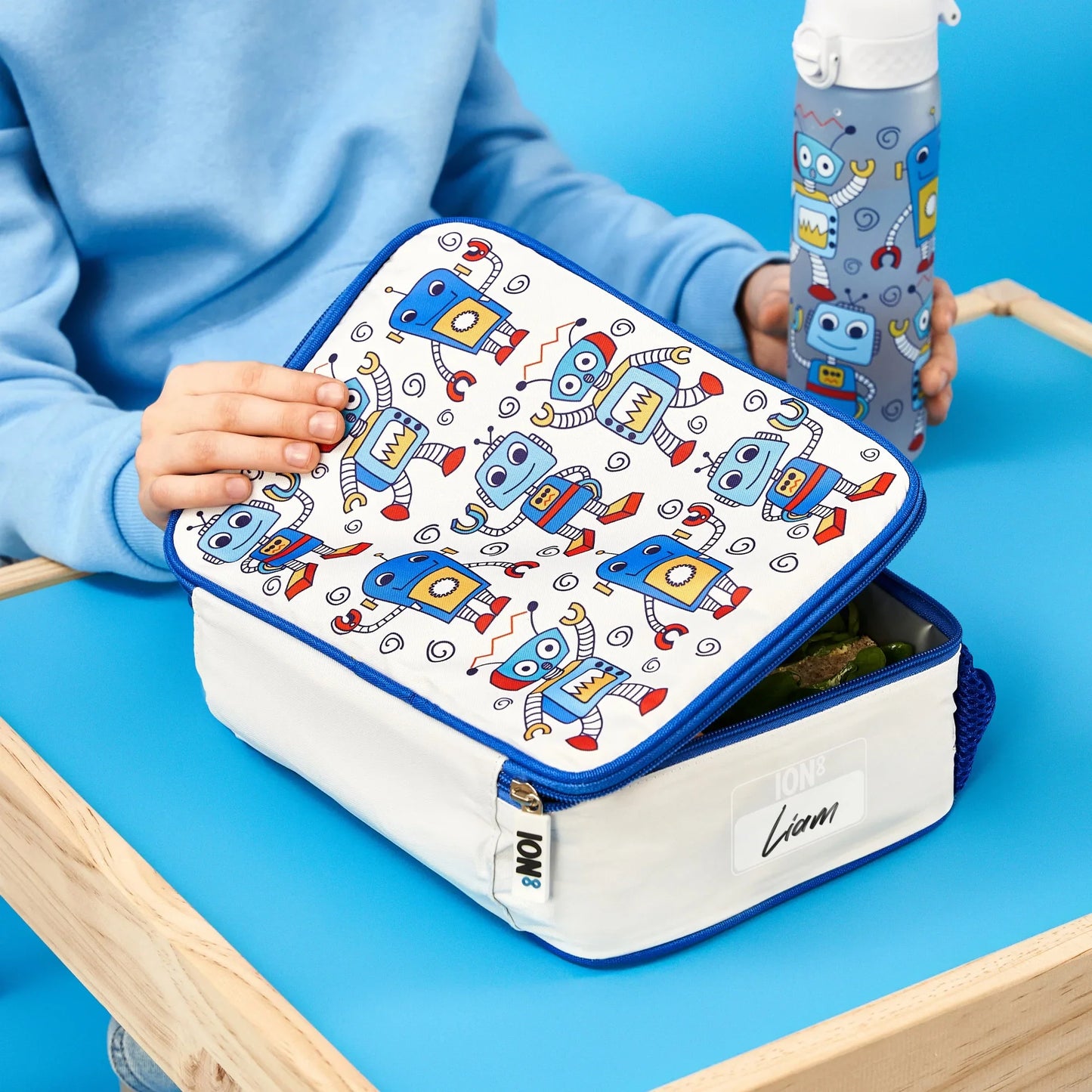 Lunch box with robot pattern held by a child on a blue table