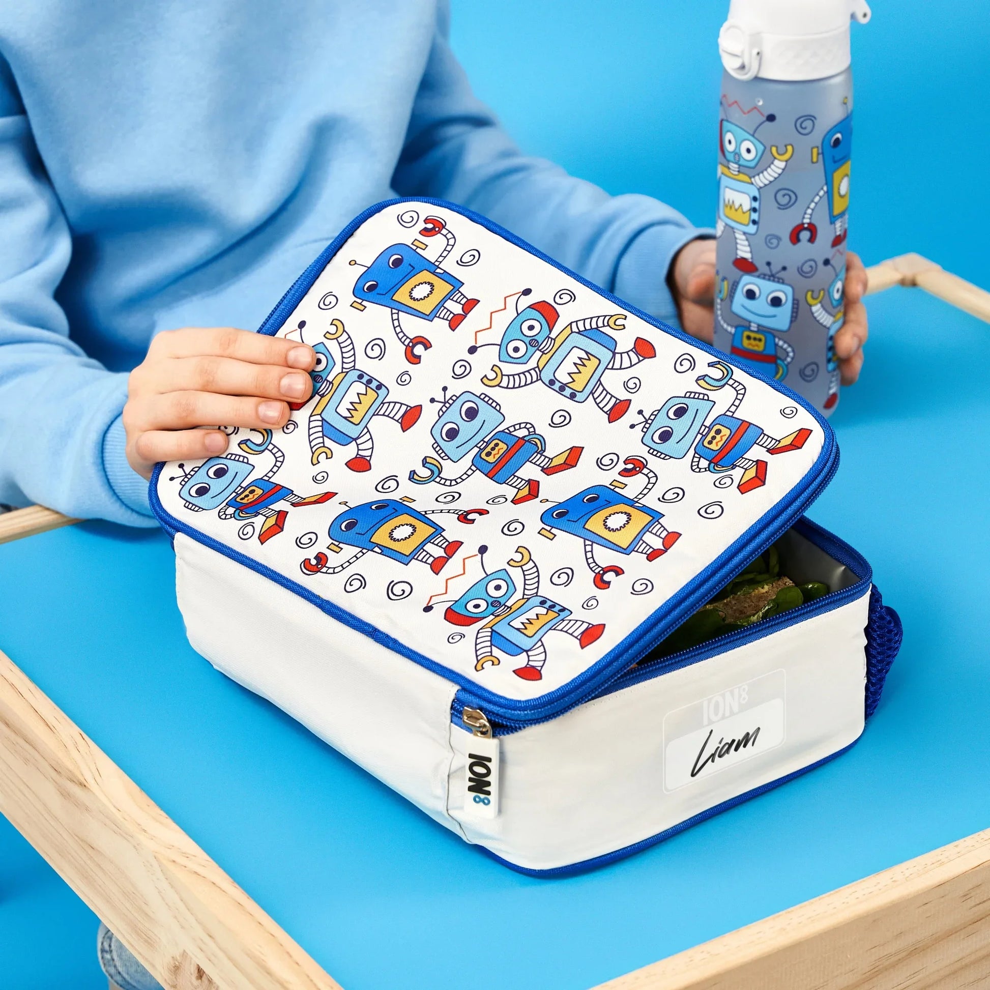 Lunch box with robot pattern held by a child on a blue table